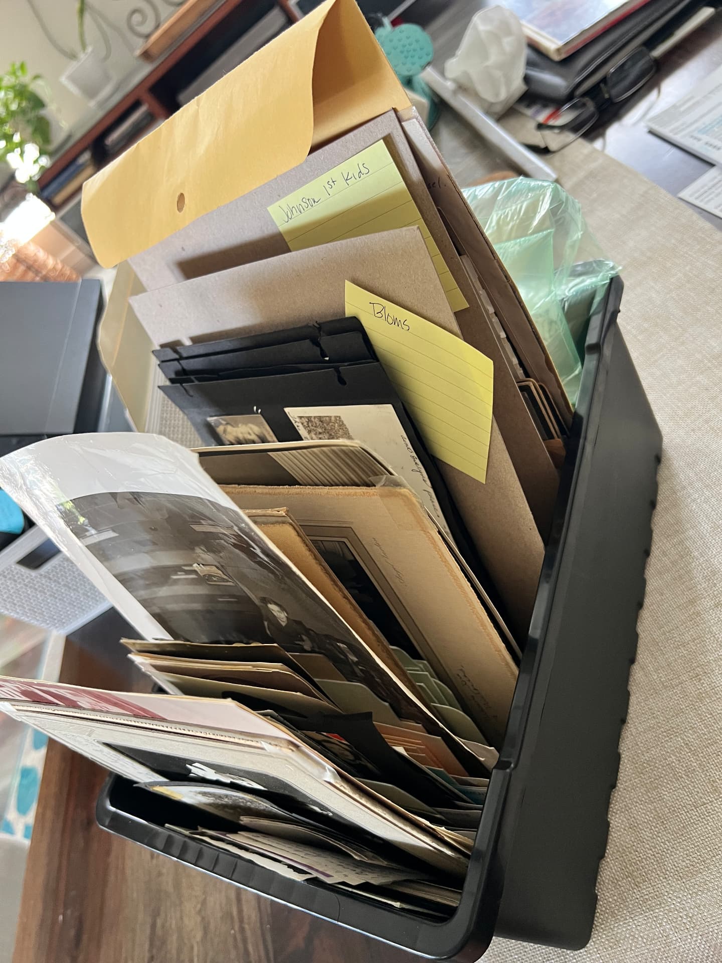 Black plastic bin overflowing with loose unlabeled family photo prints, folders and sticky notes before organizing