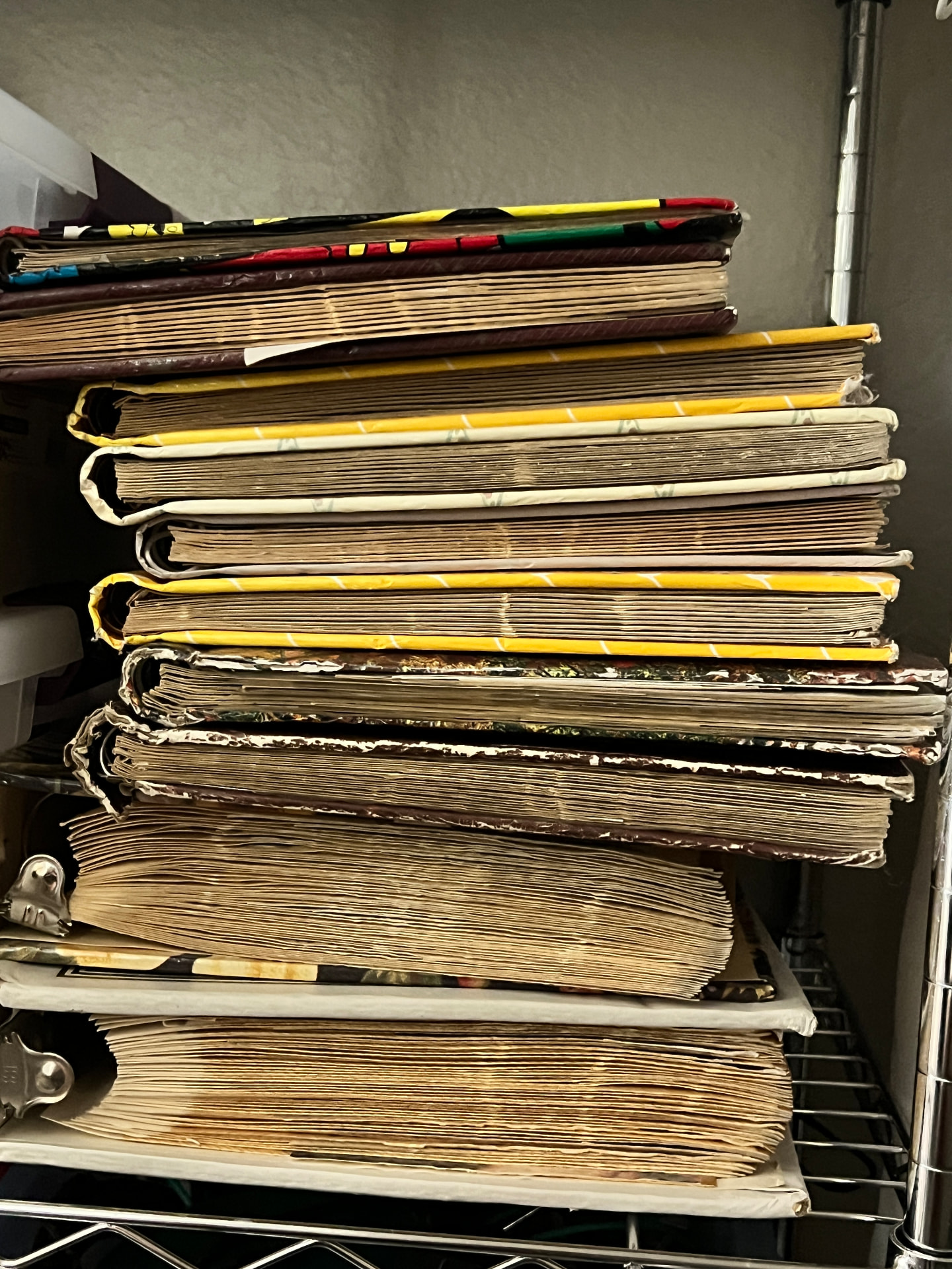 Tall stack of worn 1970s magnetic photo albums with crumbling pages on a wire shelf